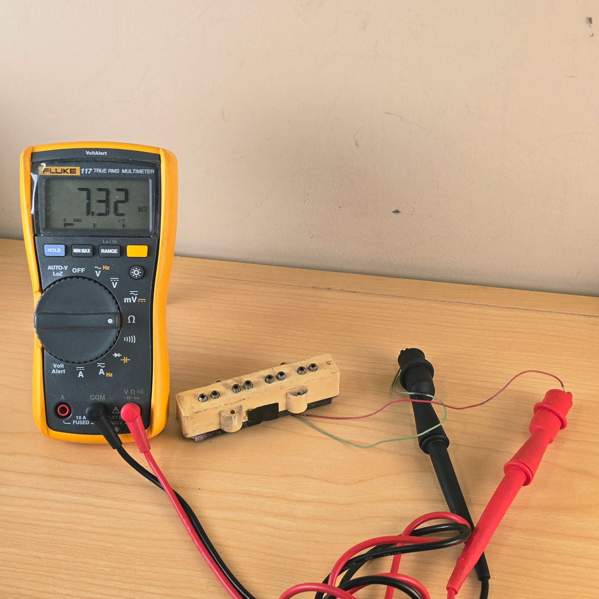 Fluke multimeter measuring 7.32 kΩ DC resistance on a cream bass pickup.
