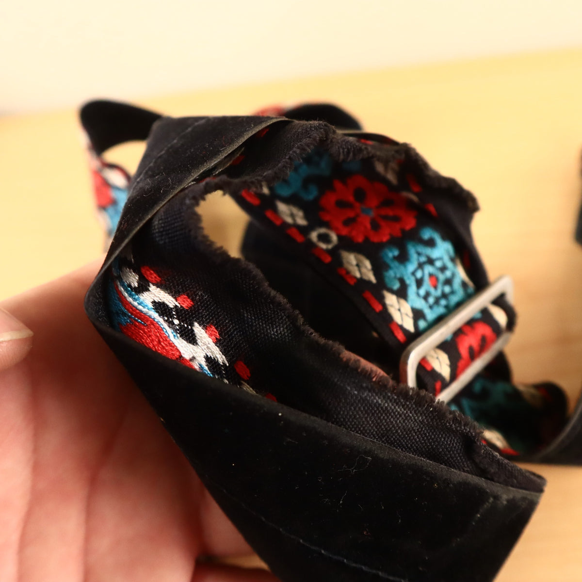 Hand holding folded guitar strap showing metal adjustment slider and fraying.