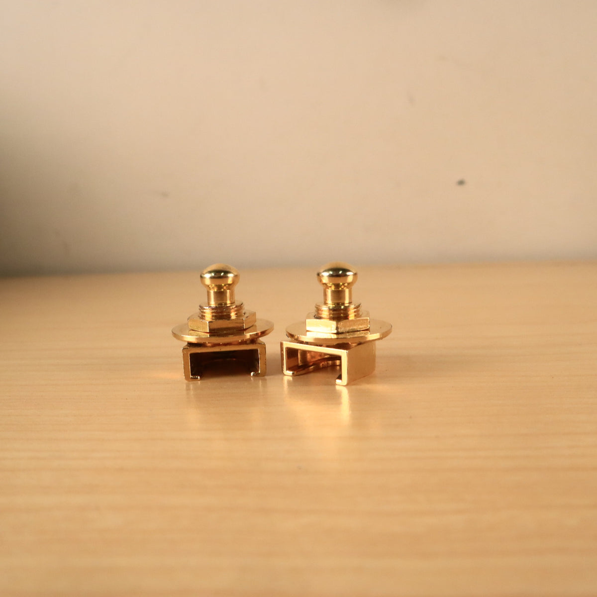 Profile view of two gold Schaller strap lock mechanisms resting on a wooden surface.