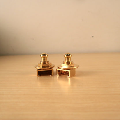 Profile view of two gold Schaller strap lock mechanisms resting on a wooden surface.