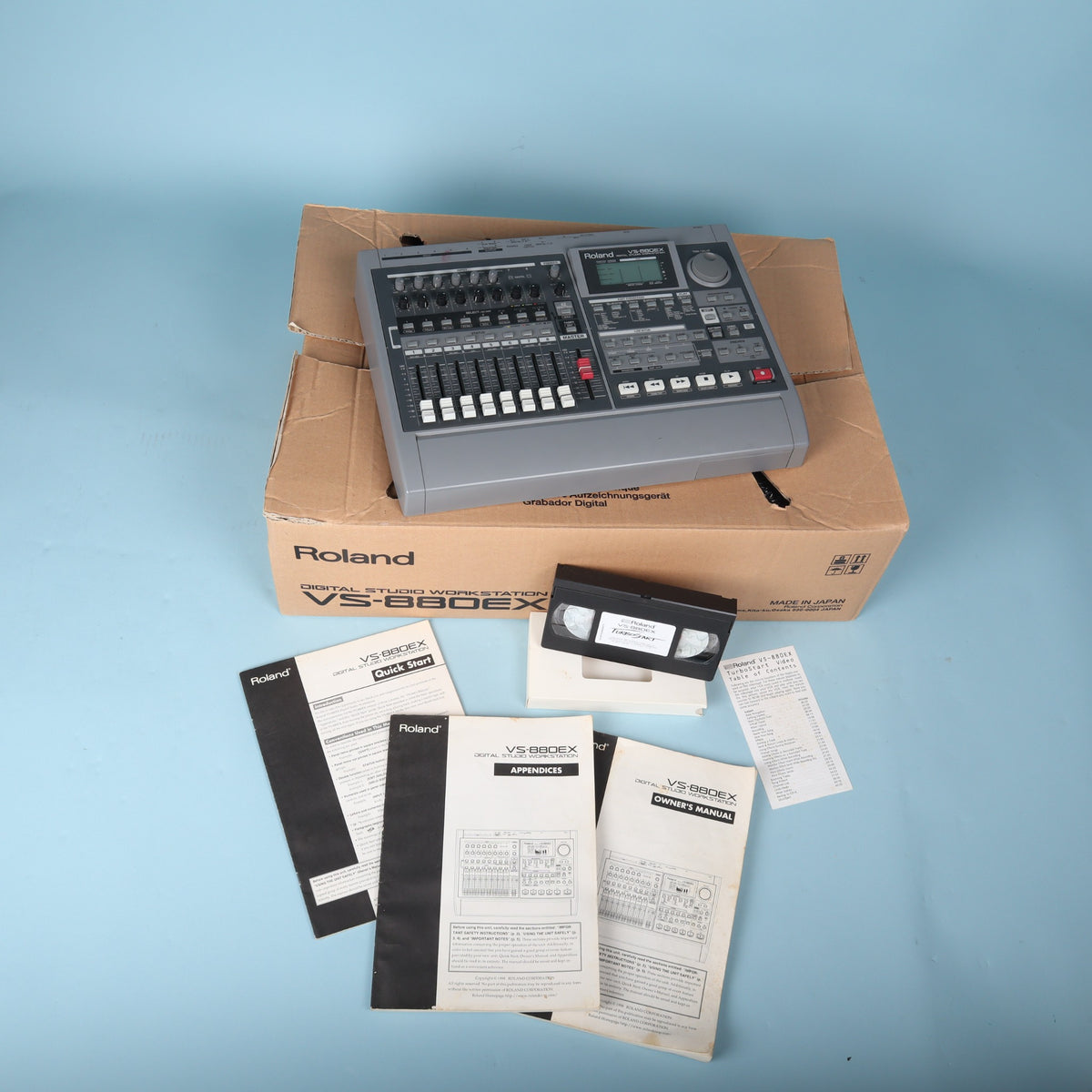Overhead view showing Roland VS-880EX 8-track recorder with user documentation and video tutorial tape.