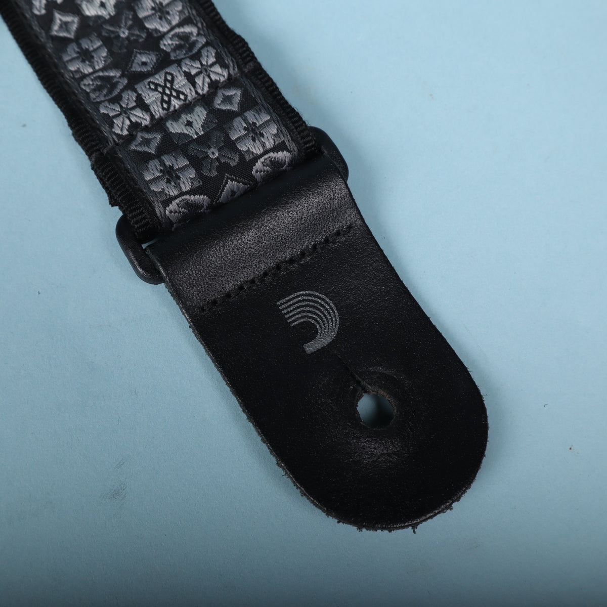 Close-up of the black leather end tab with stamped D'Addario wave logo and button hole.