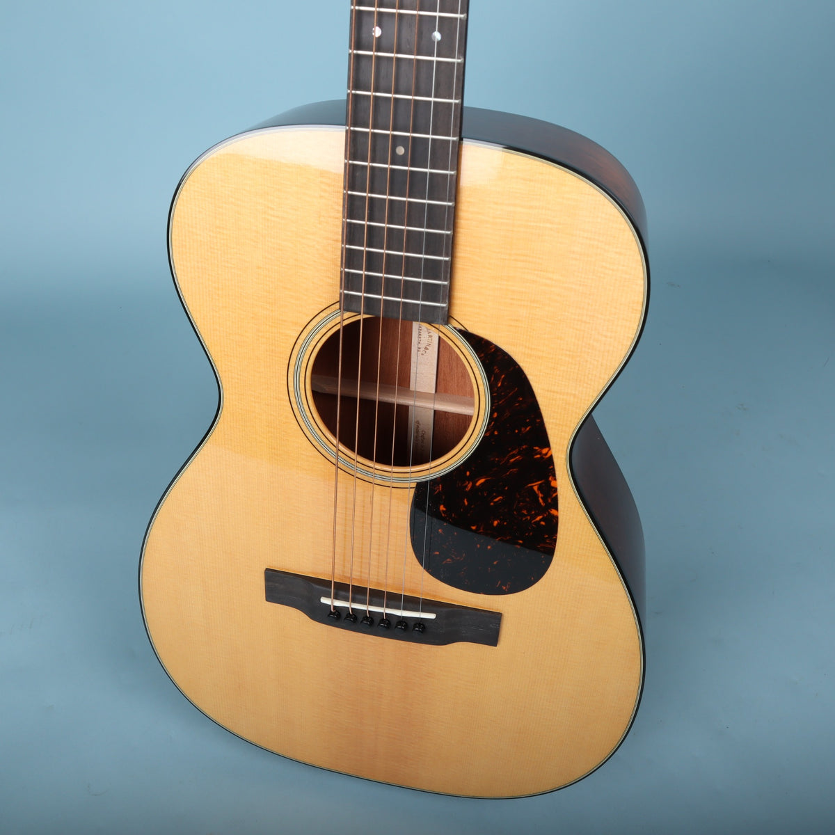 Angled close-up of the soundboard, multi-stripe rosette, pickguard, and ebony bridge on the Martin 0-18.