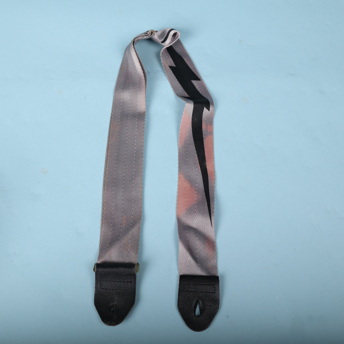 Full view of the 1980s grey guitar strap with black lightning bolt graphic and leather ends.