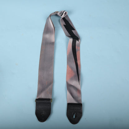 Full view of the 1980s grey guitar strap with black lightning bolt graphic and leather ends.