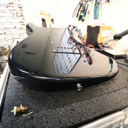 Angled rear view of black guitar body on work bench edge.
