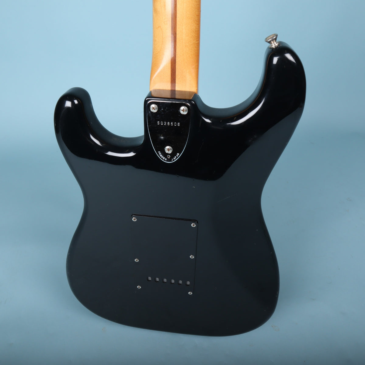 Close-up of rear neck plate stamped SQ28506 and Fender Japan on blue background.