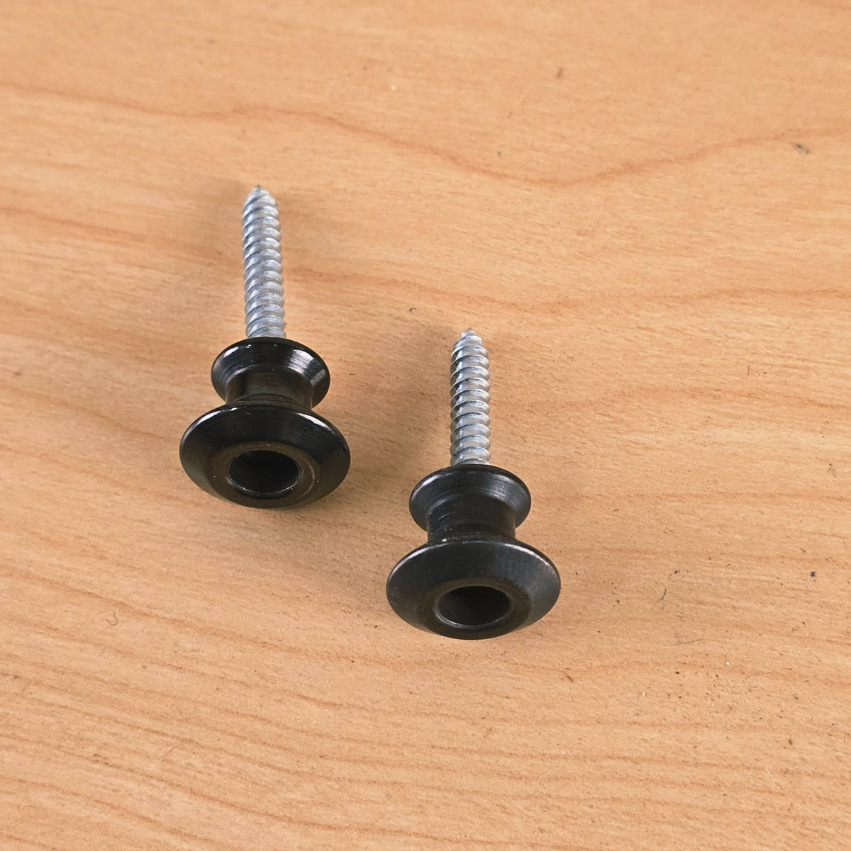 Angled top view of two black Dunlop Straplok strap buttons showing mounting screws