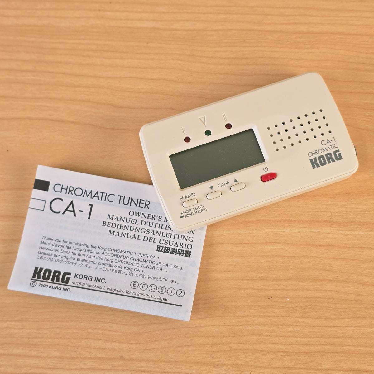 Flat overview of the Korg CA-1 chromatic tuner with the manual positioned alongside.