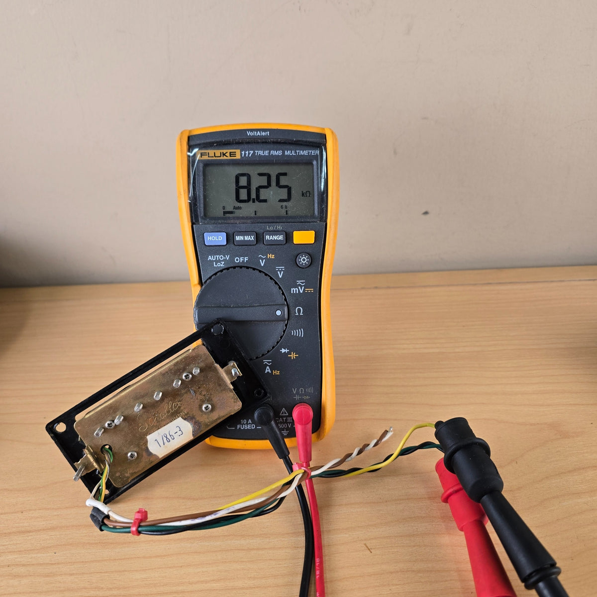Schaller humbucker baseplate connected to a Fluke multimeter showing an 8.25 kilo-ohm reading
