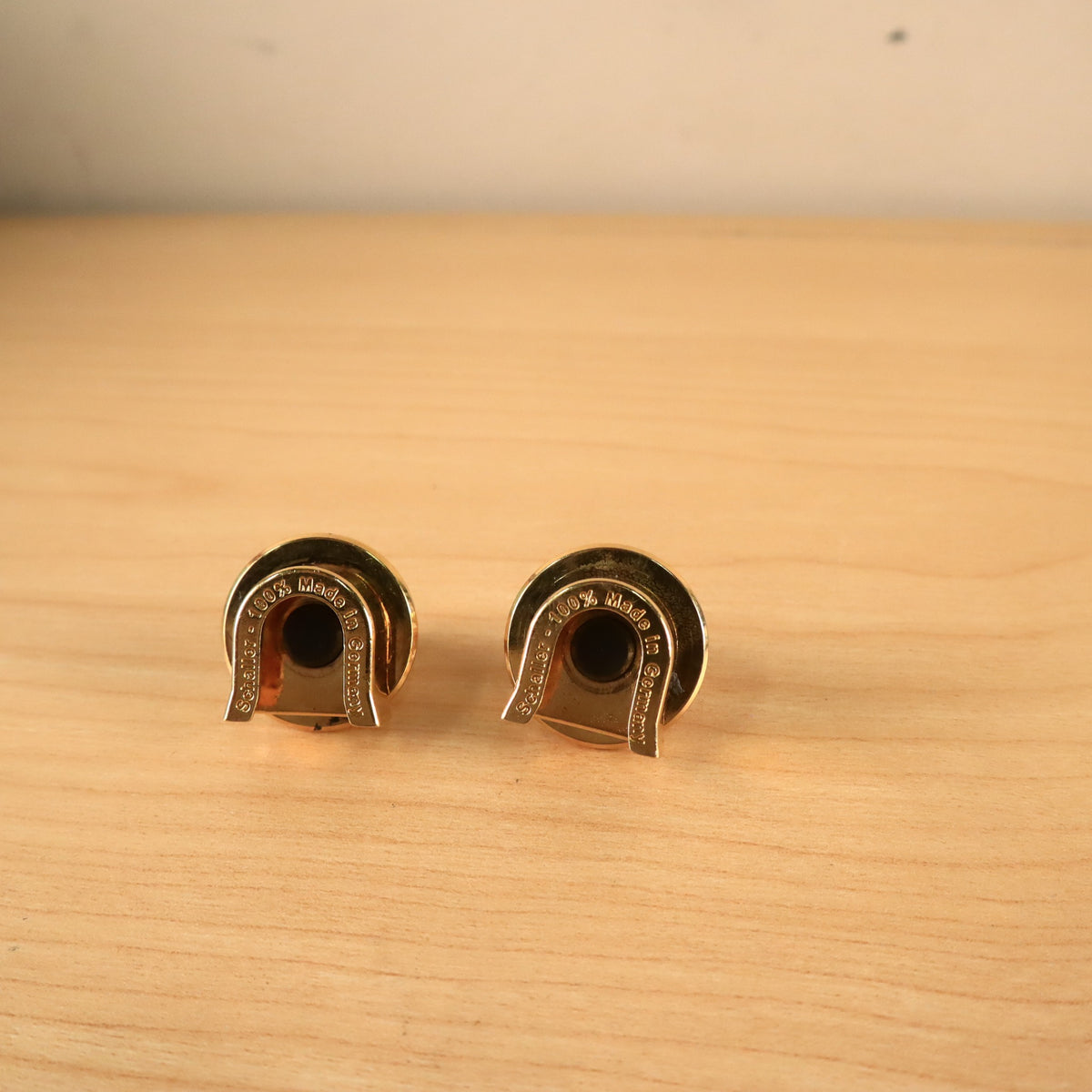 Bottom view of two gold Schaller strap locks showing 'Schaller - 100% Made in Germany' stamped lettering.
