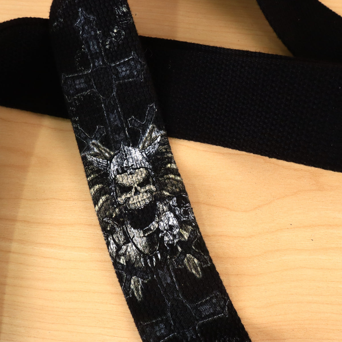 Close-up of the winged skull and cross graphic printed on the woven strap.