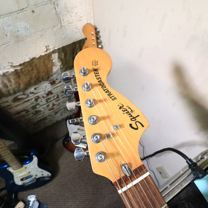 Close-up of headstock front showing Squier Stratocaster logo and string trees.