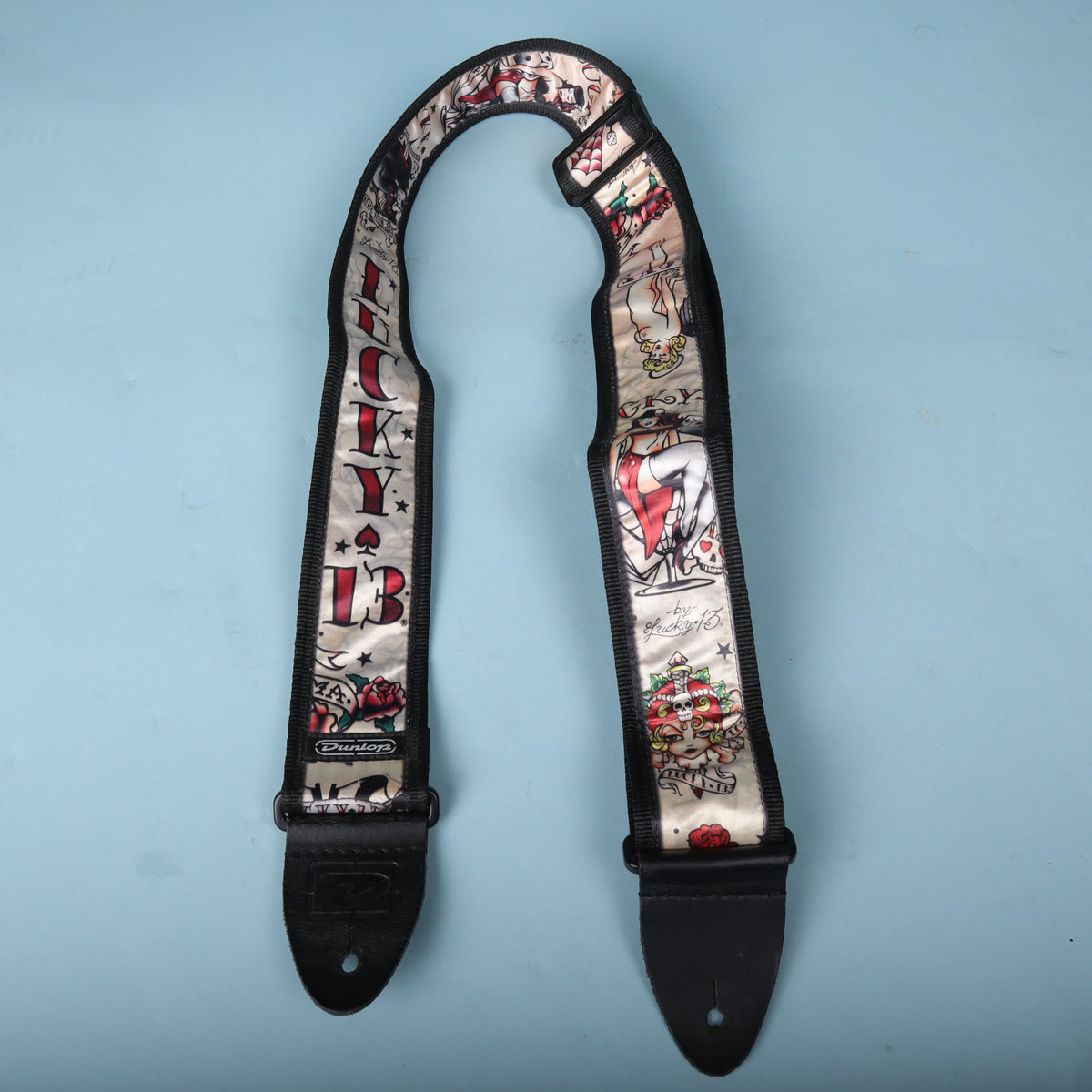 Dunlop Lucky 13 Japan Tattoo guitar strap displayed in a loop against a blue background