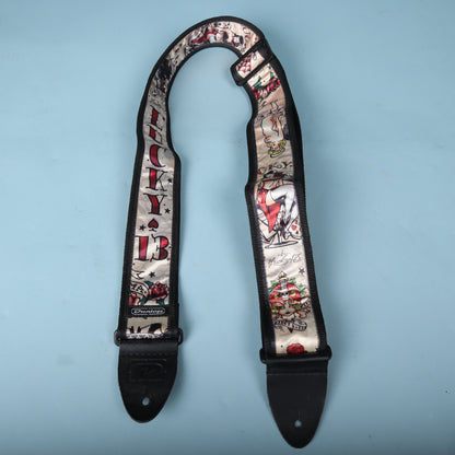 Dunlop Lucky 13 Japan Tattoo guitar strap displayed in a loop against a blue background