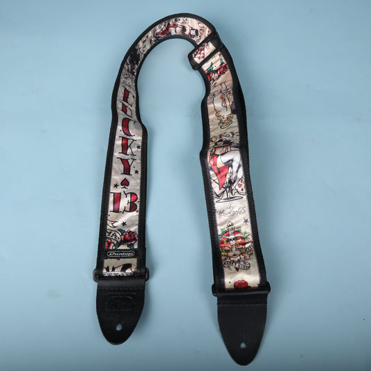 Dunlop Lucky 13 Japan Tattoo guitar strap displayed in a loop against a blue background