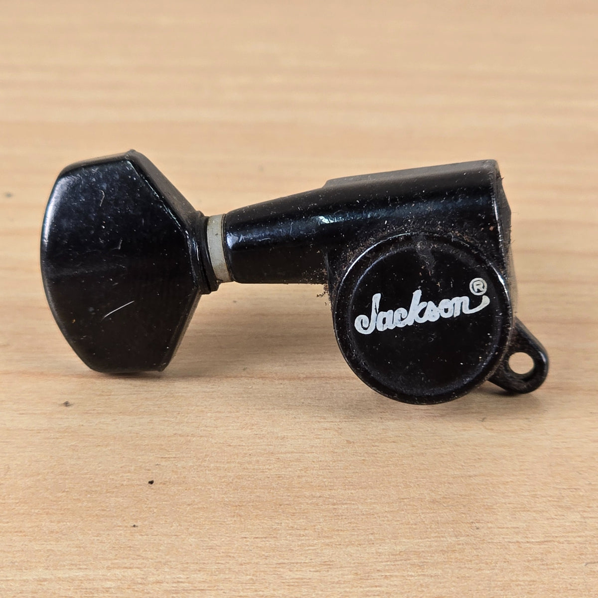 Rear casing view of a black Jackson branded guitar tuning machine showing the script logo and button.