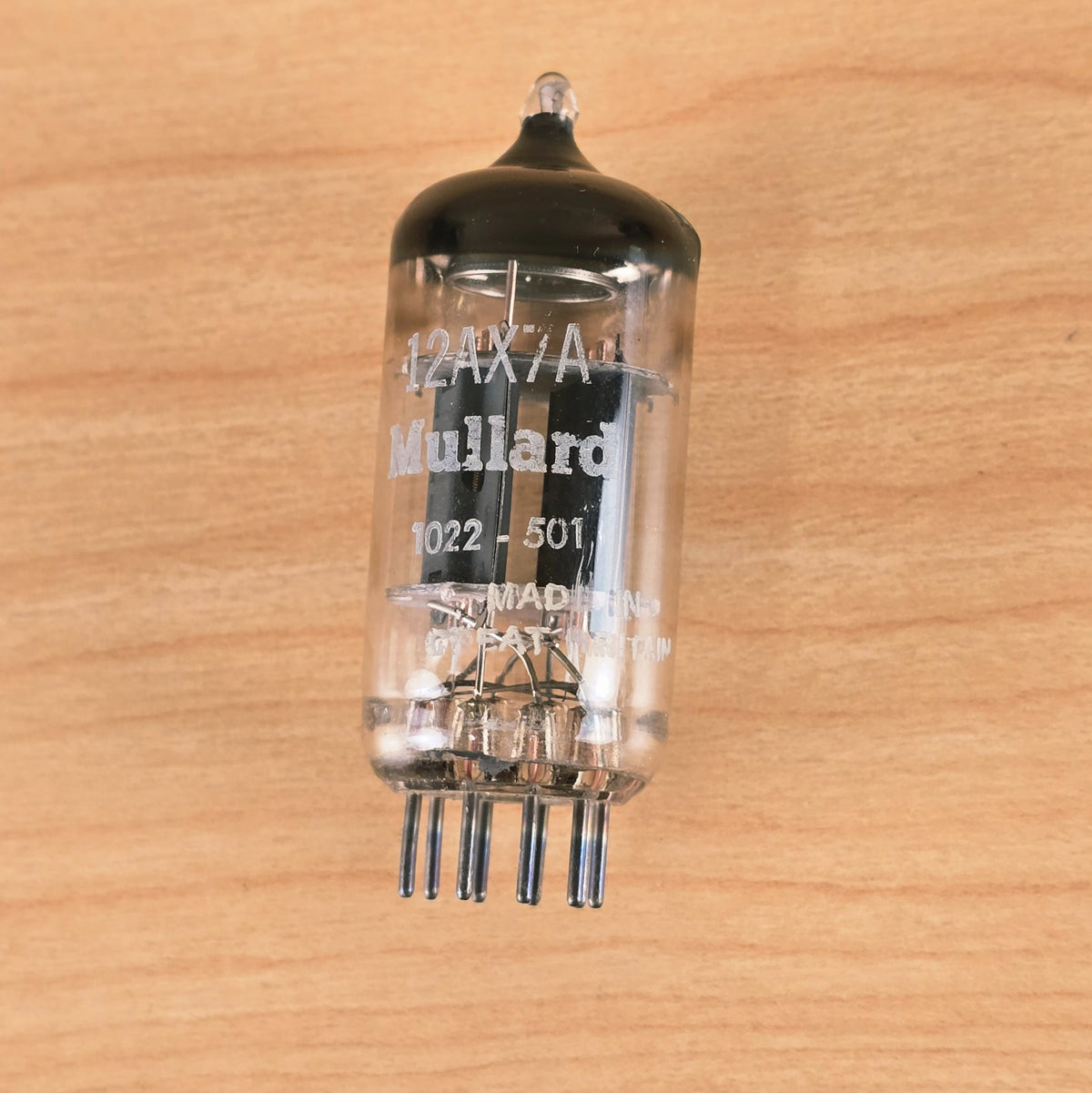 Front view of Mullard 12AX7A vacuum tube showing white print labels and internal structure on wood background.