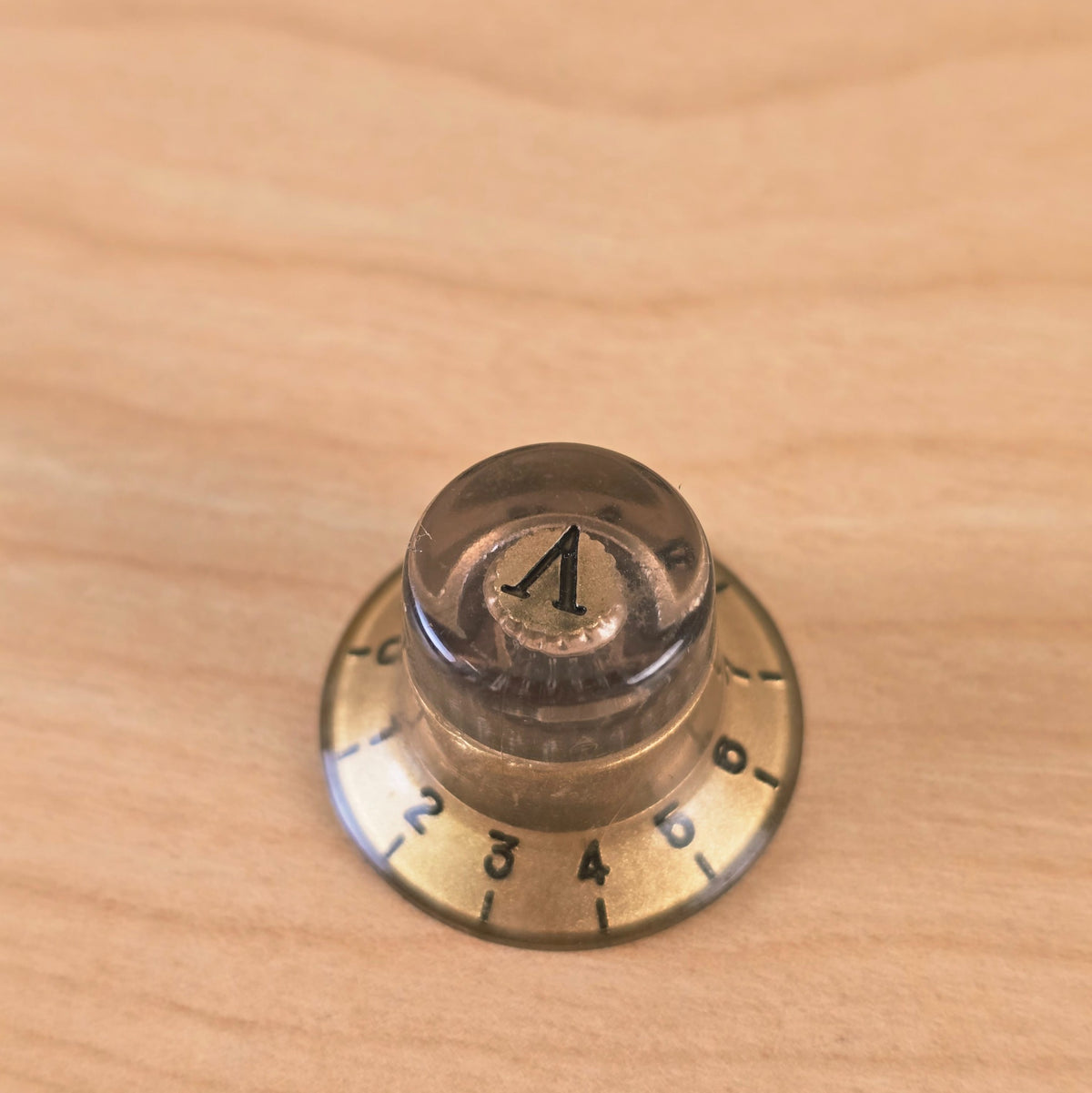 Top view of gold and transparent top hat knob with A marker on wooden surface