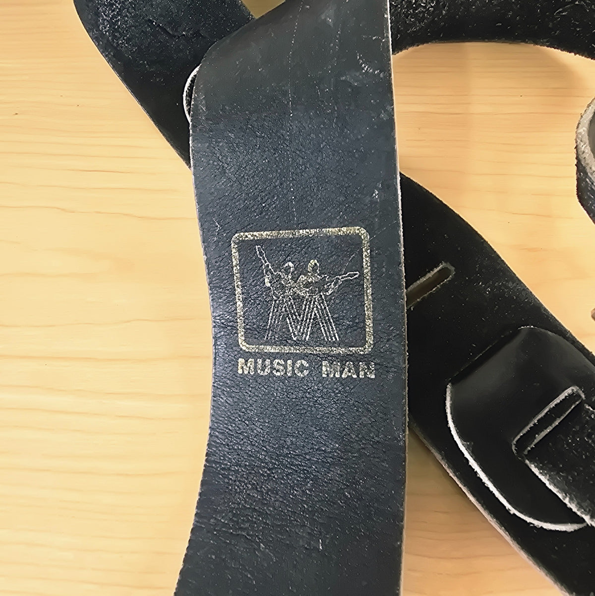 Close-up of gold-foil stamped vintage Music Man logo on black leather strap
