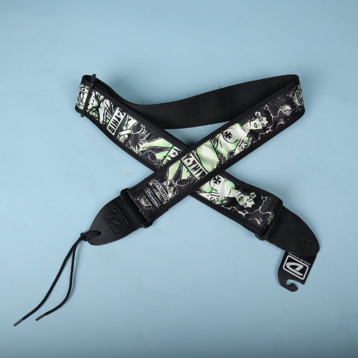 Dunlop Lucky 13 Dead Island guitar strap laid out in an X pattern against a light blue backdrop.