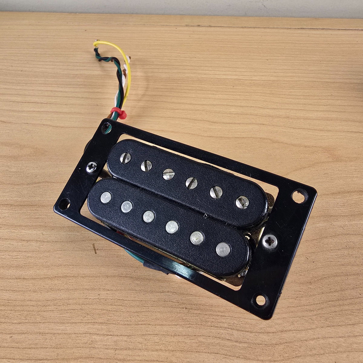 Angled top-down view of black Schaller humbucker pickup with mounting hardware