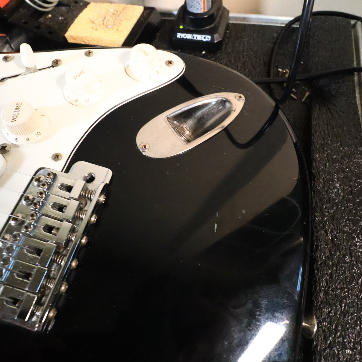 Close-up of black body finish showing bridge, volume knob, tone knobs, and output jack.