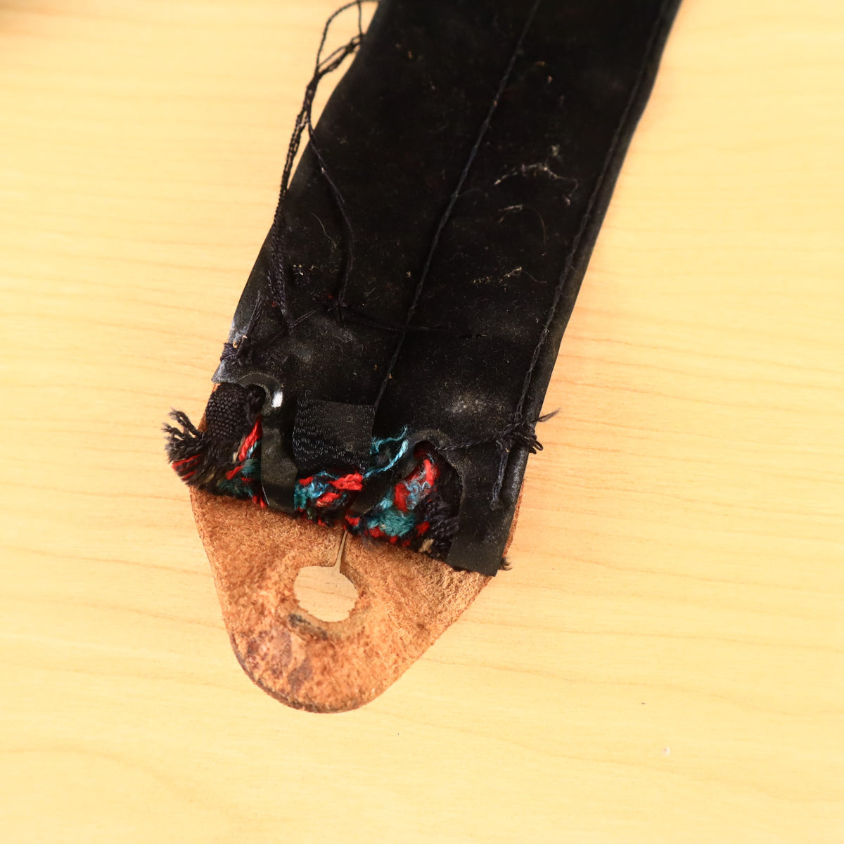 Close-up of worn leather end tab and frayed backing material.