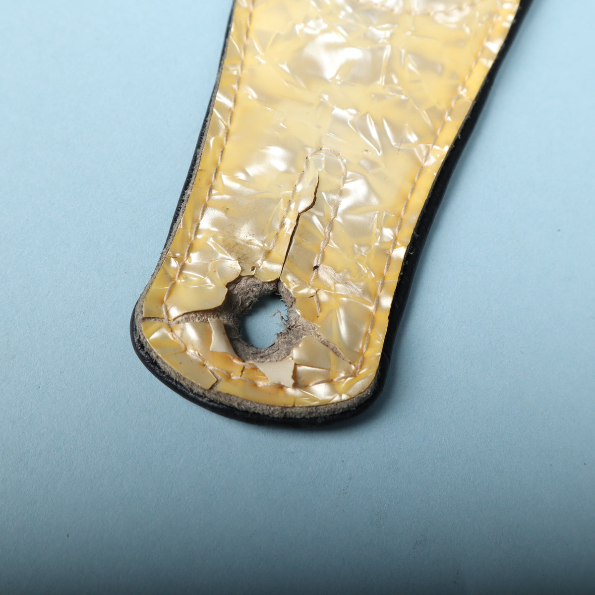 Detailed view of the strap button hole with cracking and material loss in the pearloid overlay.