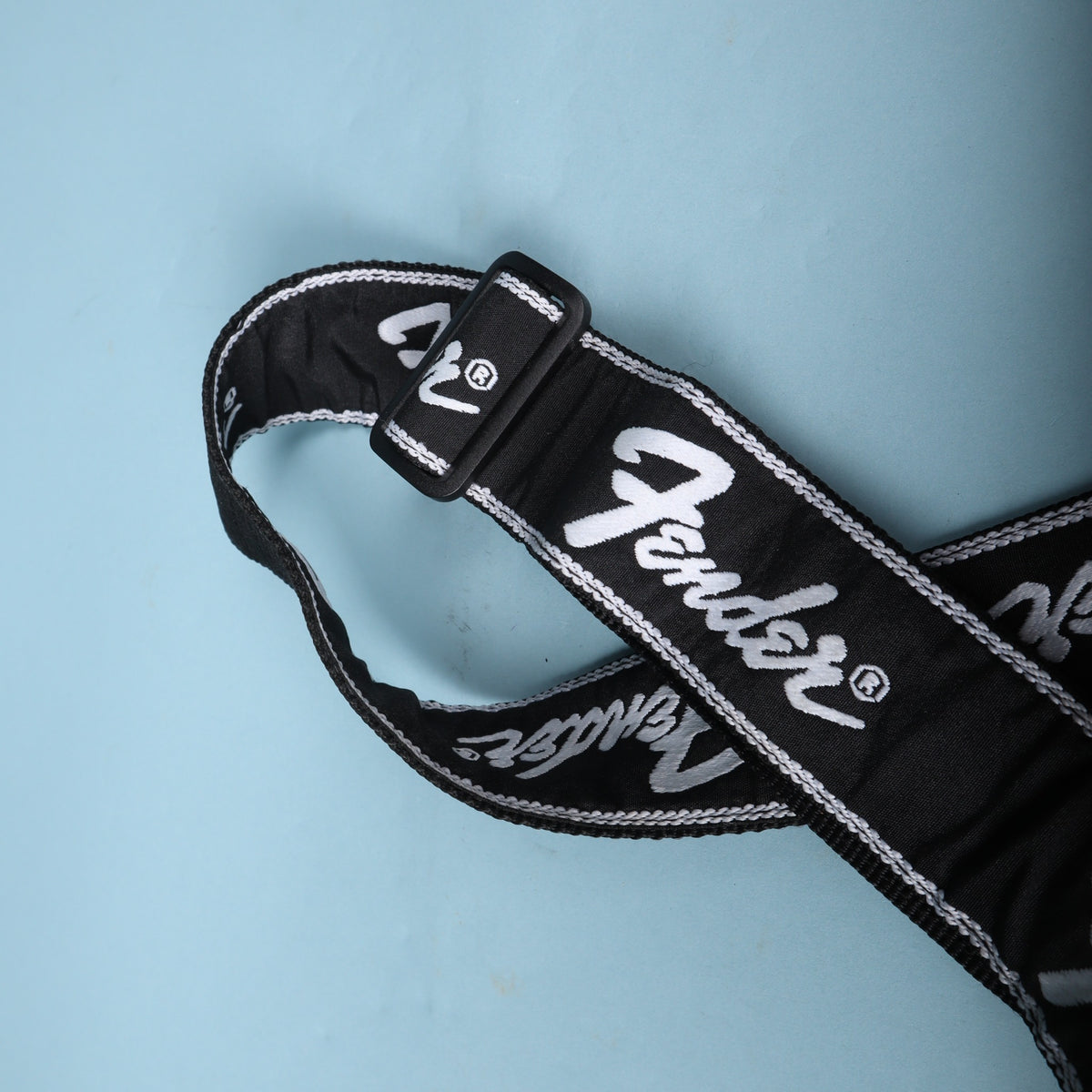 Black plastic adjustment buckle on a Fender running logo strap with embroidered white script