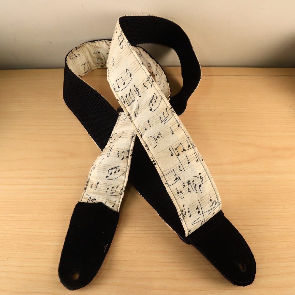 Crossed arrangement of the sheet music pattern guitar strap displaying both black suede end tabs.