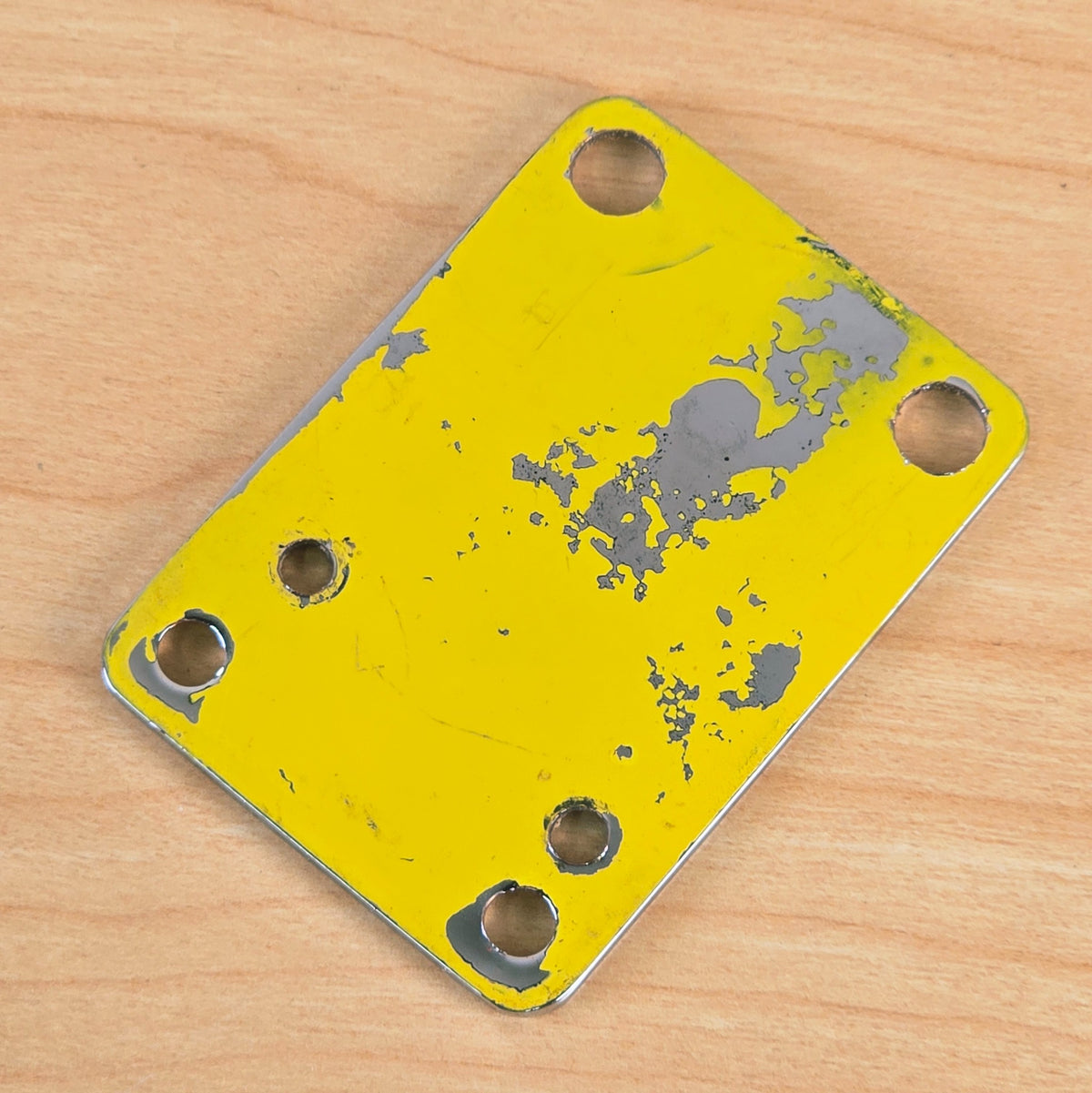 Back side of the Danelectro neck plate showing peeling yellow backing material and metal finish.