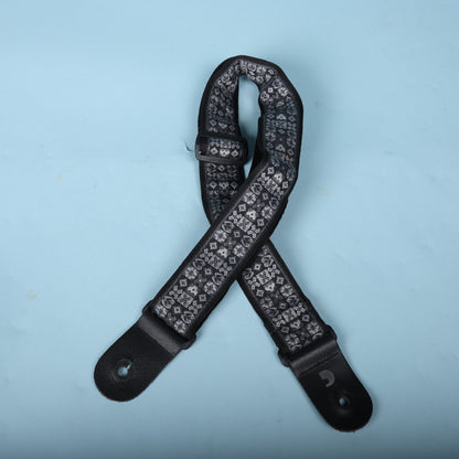 D'Addario grey and black woven jacquard guitar strap laid out against a blue background.