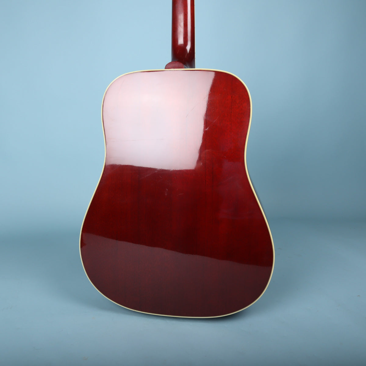 Full view of the guitar's cherry-stained back on a blue background.