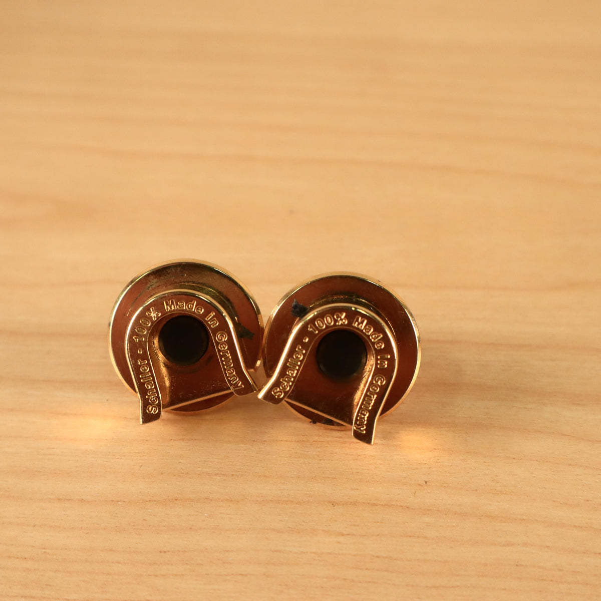 Angled underside view of two gold Schaller guitar strap lock pieces showing finish condition.