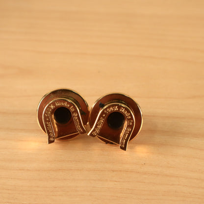 Angled underside view of two gold Schaller guitar strap lock pieces showing finish condition.