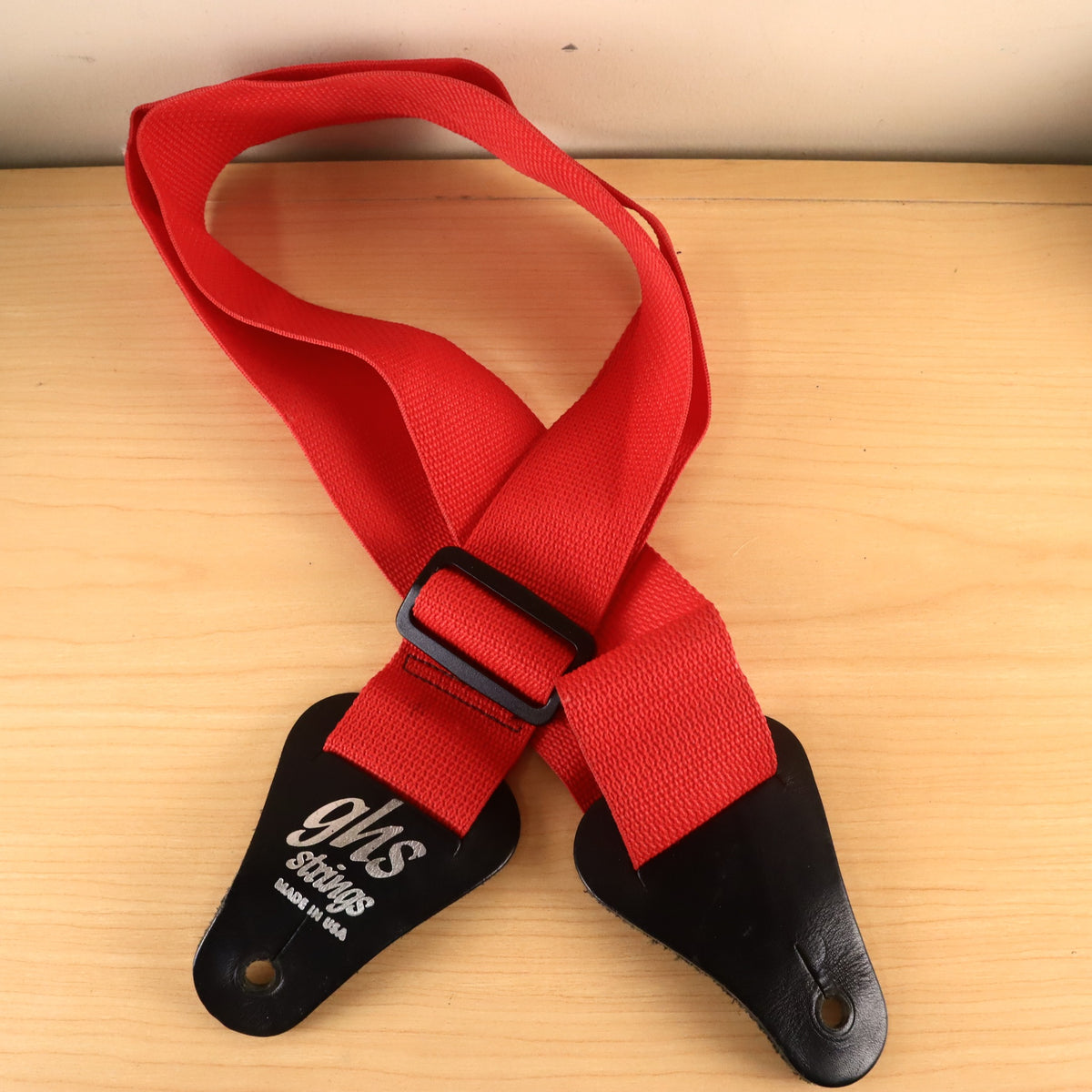 GHS red webbing guitar strap coiled on a light wood surface.