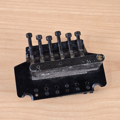 Underside view of black tremolo bridge with string locking bolts and block