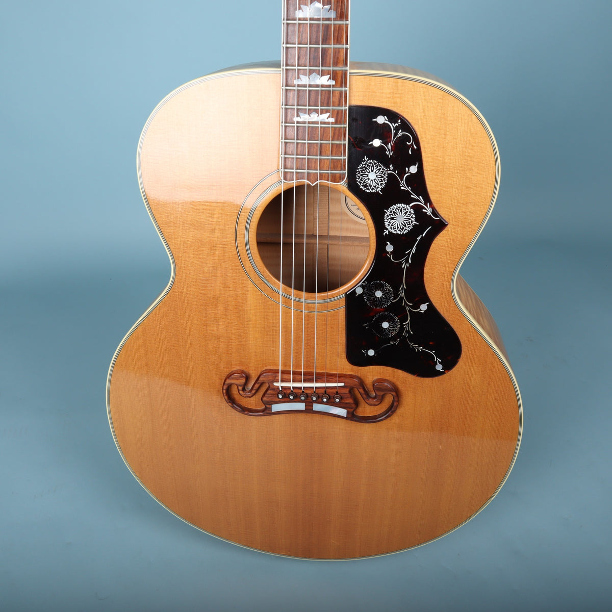 Close-up view of soundhole, floral pickguard, and rosewood mustache bridge on a Gibson J-200.