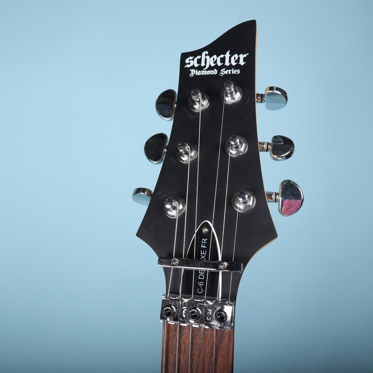 Front of the Schecter Diamond Series headstock showing the C-6 Deluxe FR truss rod cover and locking nut.