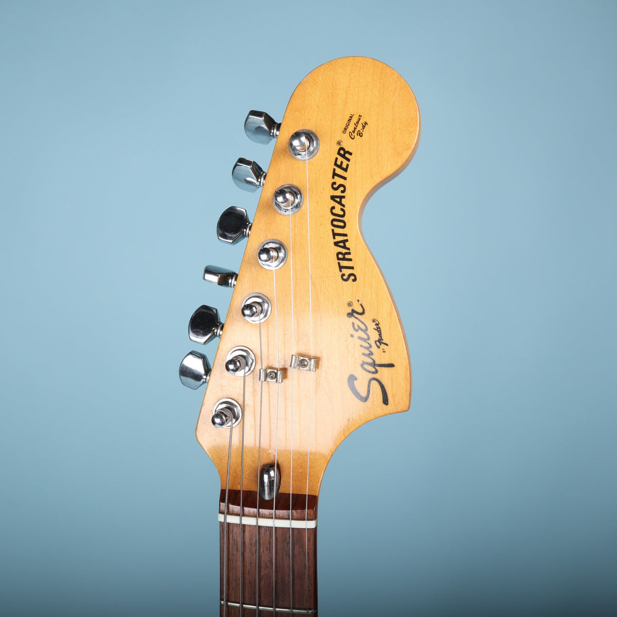Front view of headstock with Squier Stratocaster headstock logo on blue background.